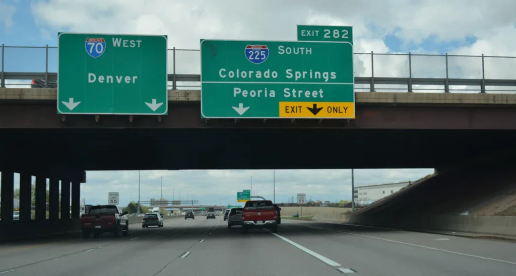 Highway overhead signs directing traffic toward I-70 West to Denver and I-225 South to Colorado Springs, a route often taken by Aurora car maintenance customers.