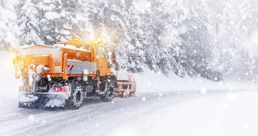 An orange snowplow clears a snow-covered road during a heavy snowfall on Ute Pass, emphasizing the importance of a clean engine air filter for high-altitude driving.