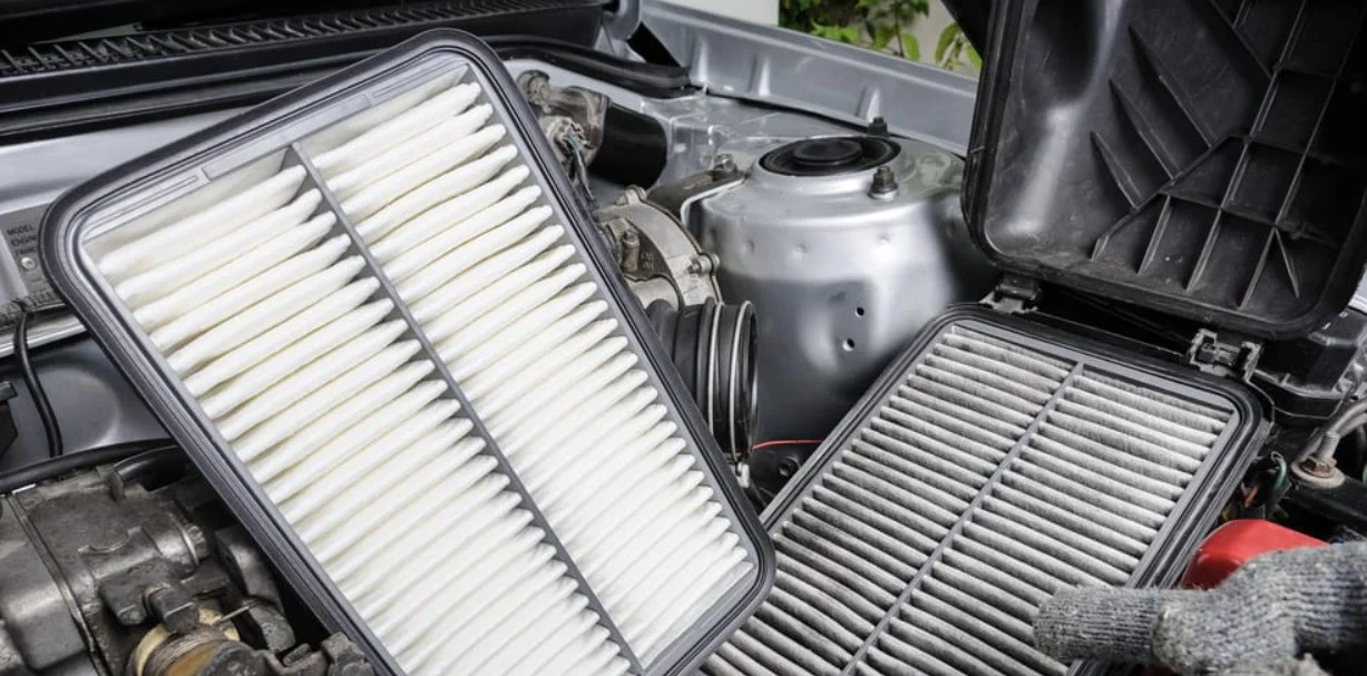 A clean rectangular car engine air filter held next to a dirty, used filter during engine air filter maintenance in Aurora.
