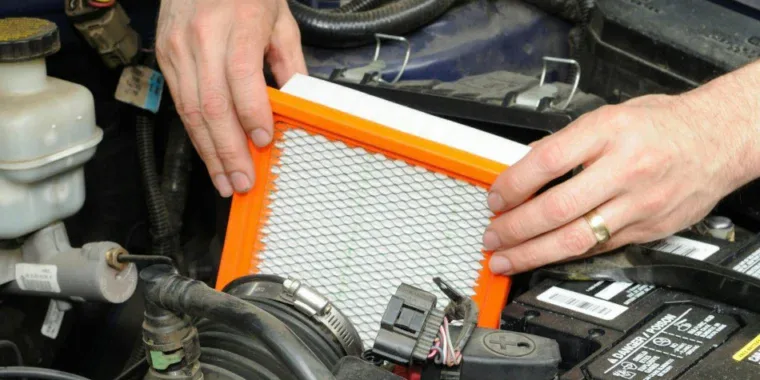 Hands holding an engine air filter over an open car air cleaner box.