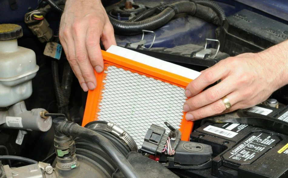 Hands holding an engine air filter over an open car air cleaner box.