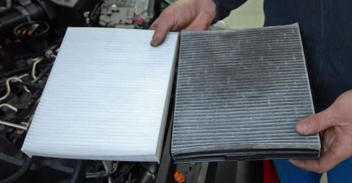 A person holding a clean, white cabin air filter next to a dirty, used one.