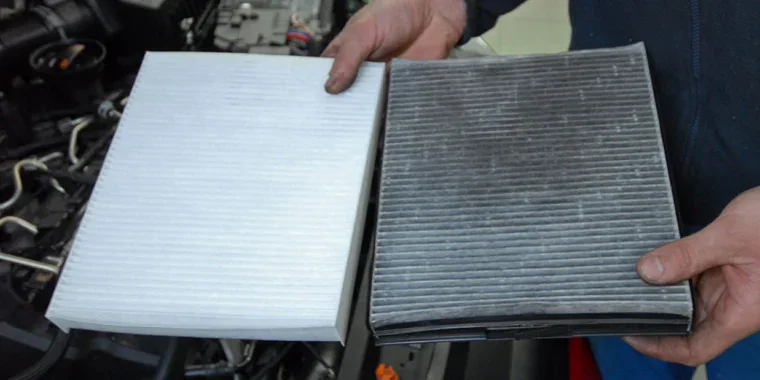 A person holding a clean, white cabin air filter next to a dirty, used one.