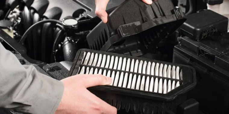 Hands removing a car engine air filter from its housing.