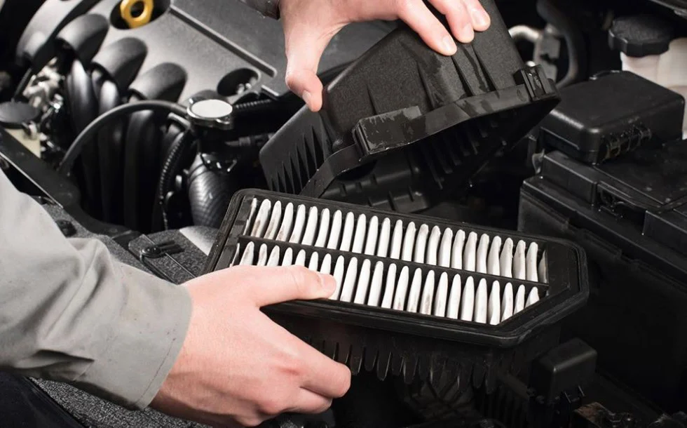 Hands removing a car engine air filter from its housing.