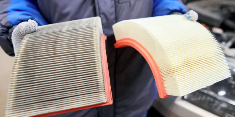 A mechanic holding a dirty used engine air filter next to a clean new one for automotive maintenance.