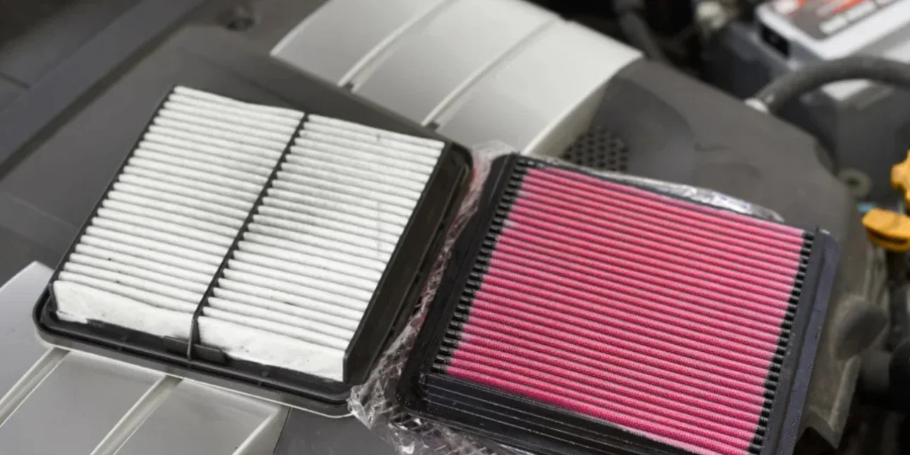 A new white paper engine air filter next to a red aftermarket performance air filter.