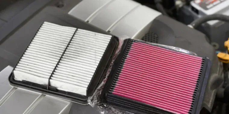 A new white paper engine air filter next to a red aftermarket performance air filter.