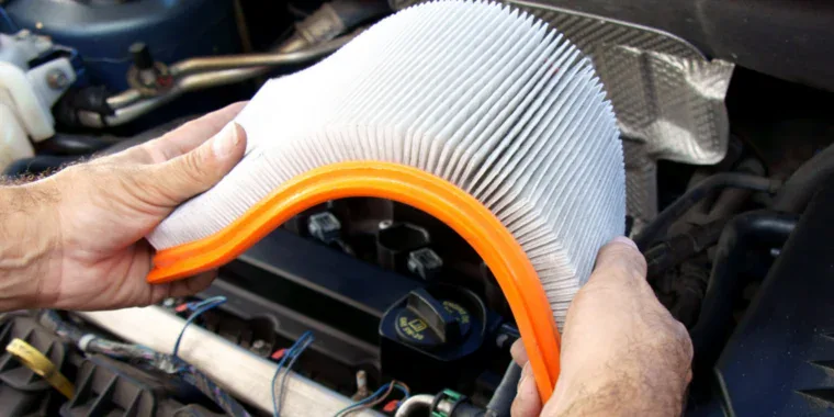 A person holds a dirty, pleated engine air filter over an open car hood, reflecting the heavy dust from Jerome wind.